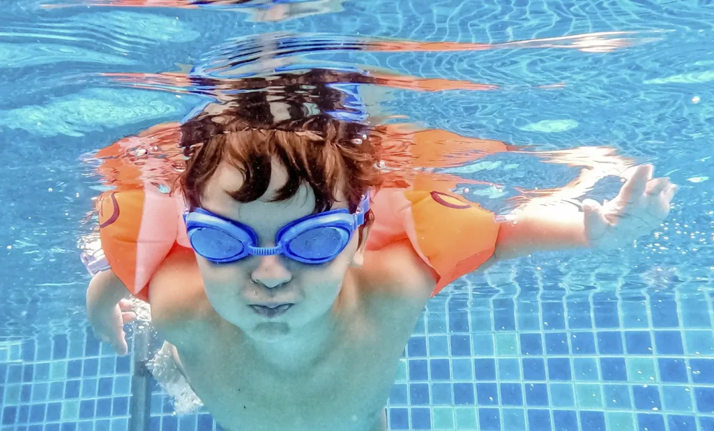 Fotografia bajo el agua de un niño pequeño con manguitos nadando